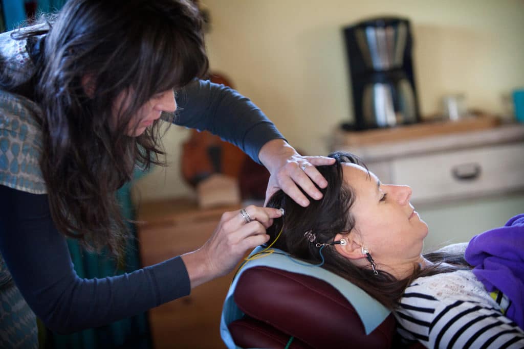 Concussion clinic technician putting neurofeedback electrodes on women's head. 